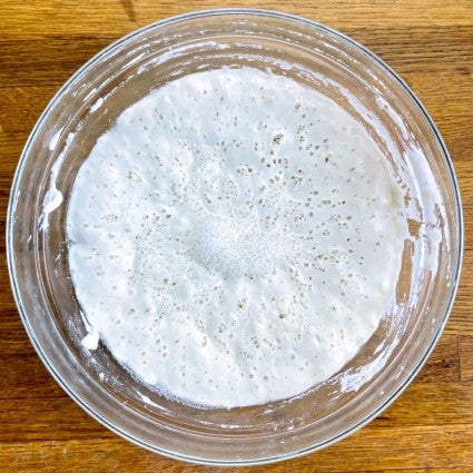 Sourdough starter in a clear glass bowl, fed 11 hours ago, showing lots of bubbles, both large and small.